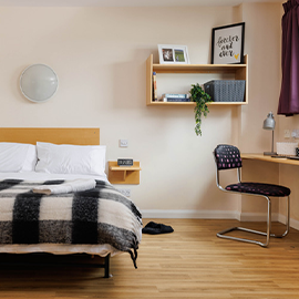 Student accommodation bedroom with bed, desk, chair, and wall shelving