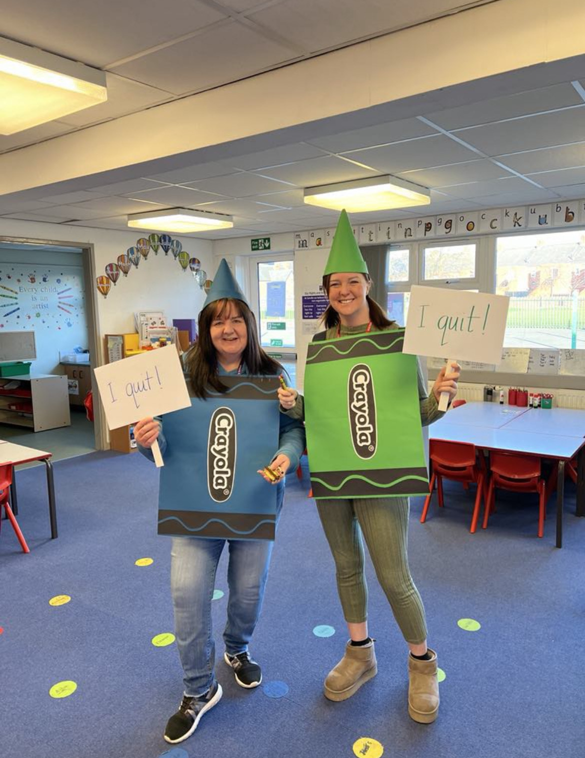 2 Women dressed as a blue and green Crayola for World Book Day smiling and holding signs that read 'I quit'