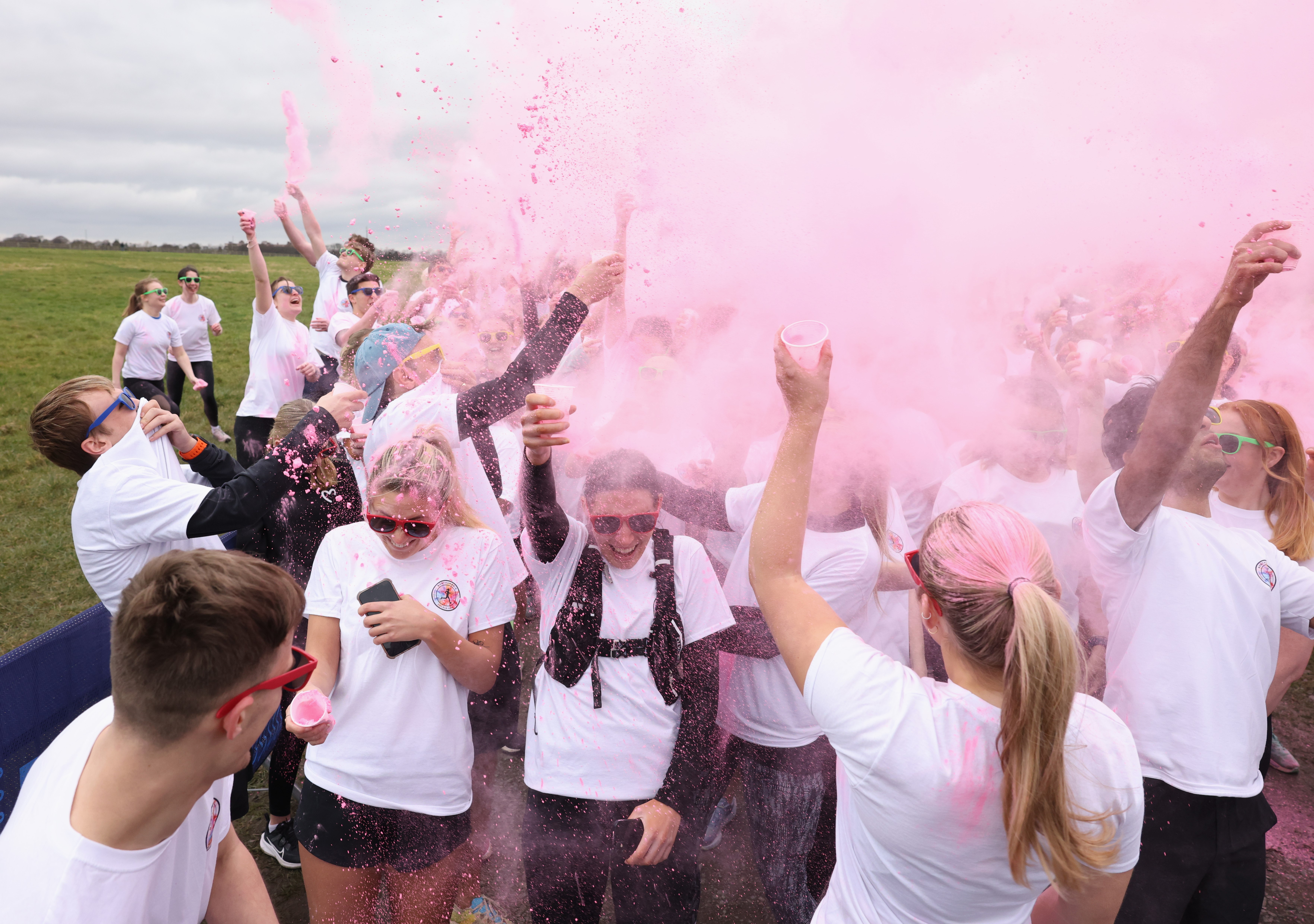 Group of people smiling celebrating finishing a run, covered in pink powder 