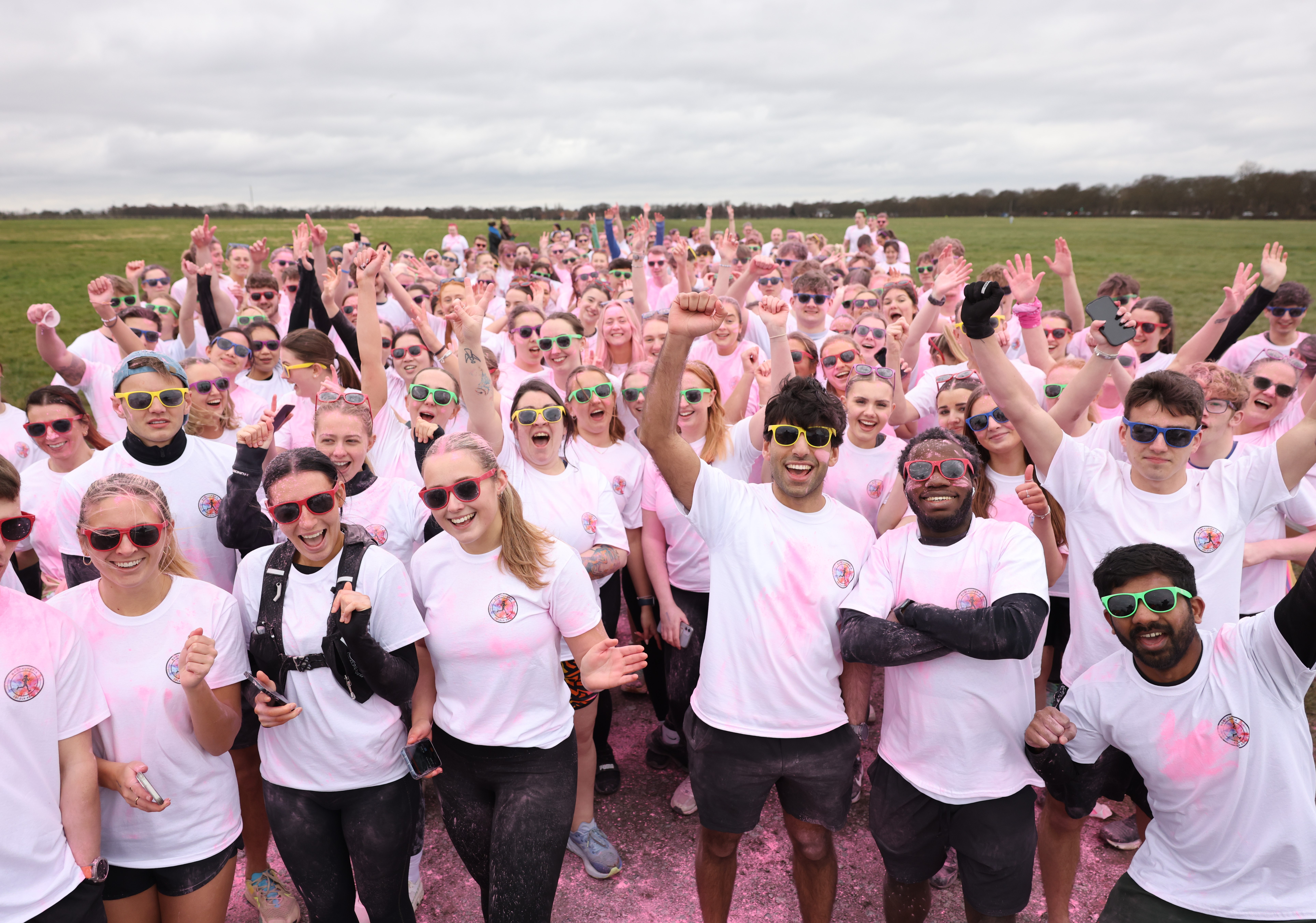 Group of people wearing white t-shirts and sunglasses covered in pink powder smiling at the camera