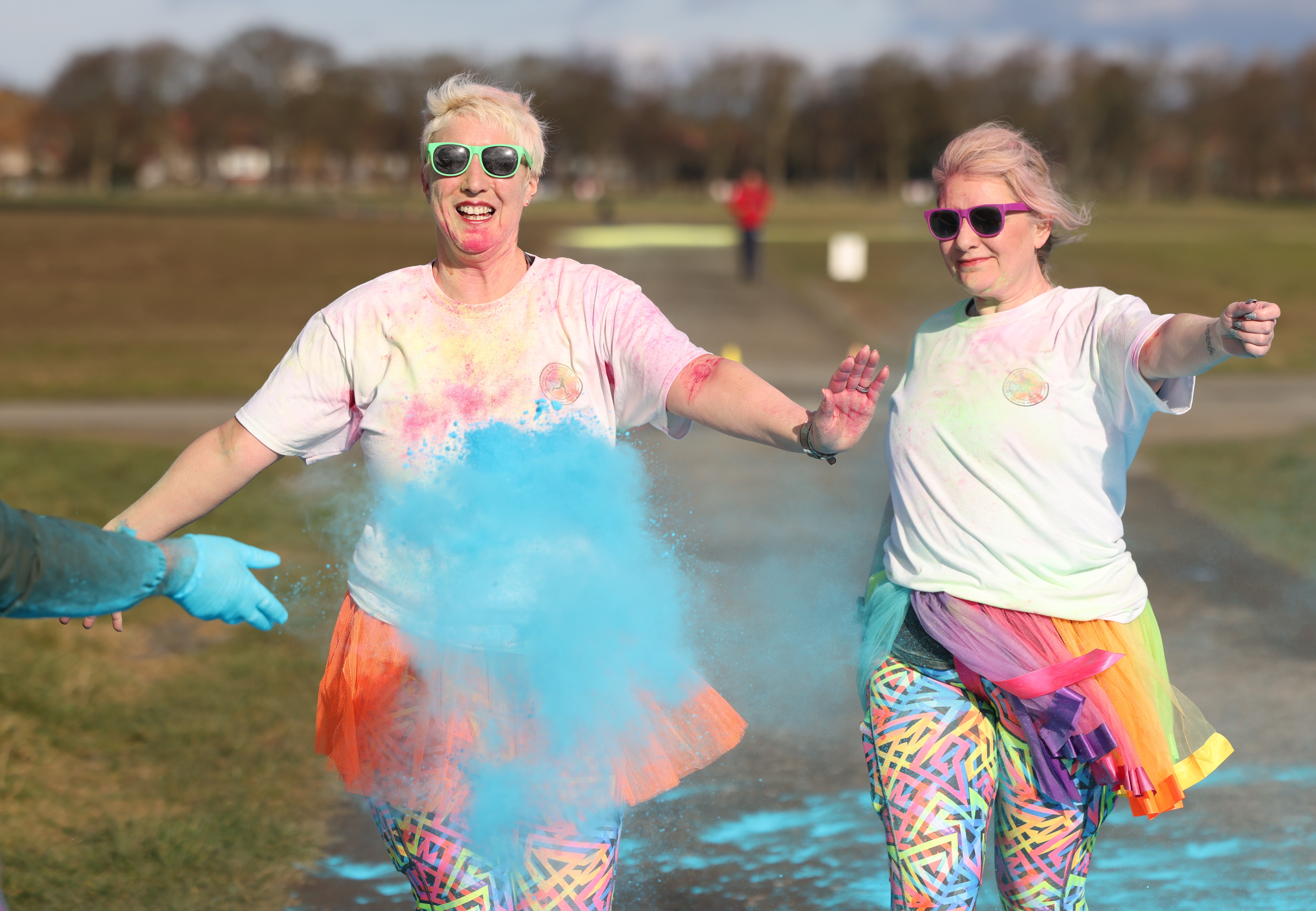 Picture of 2 women running  a colour run wearing sun glasses and smiling at the camera