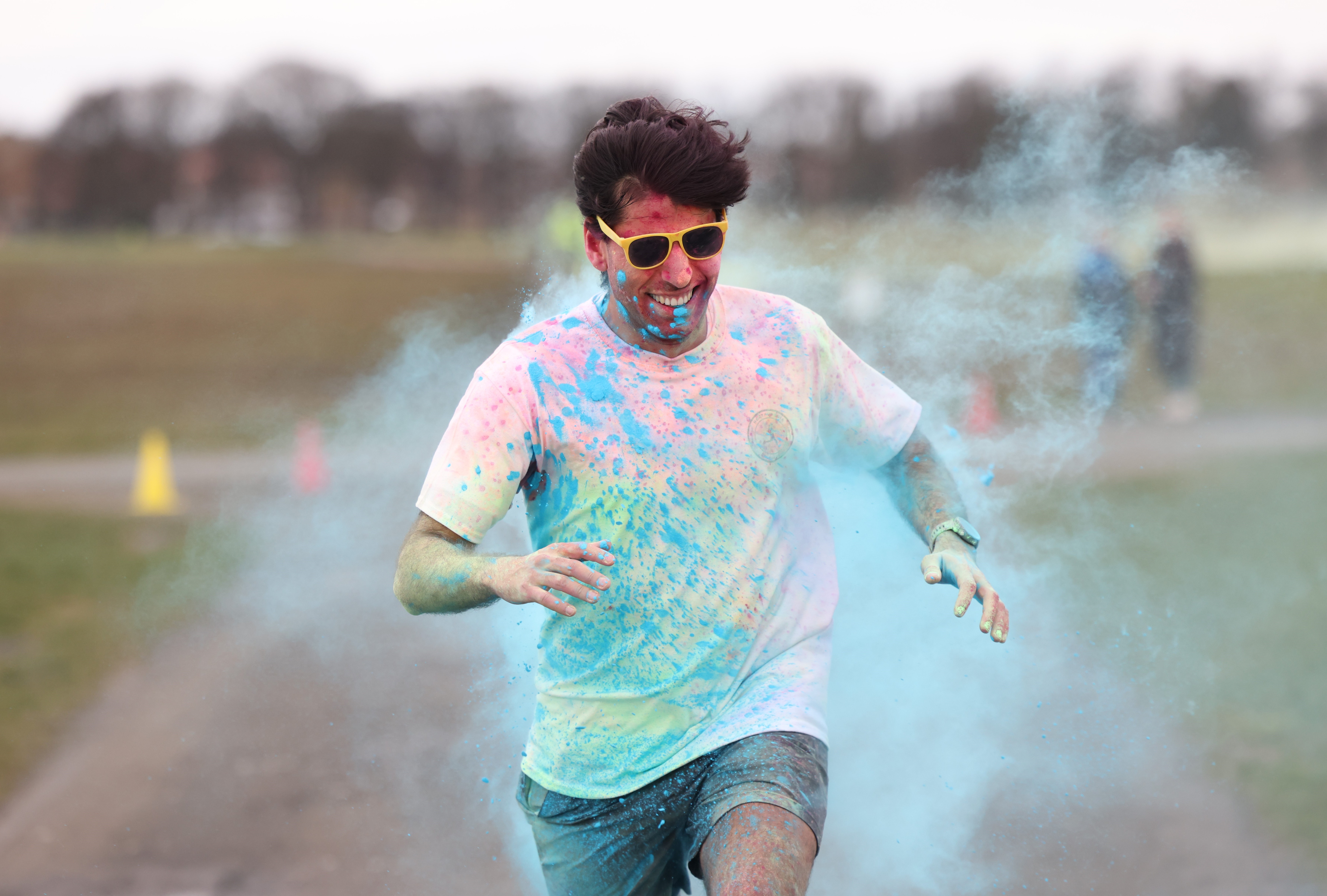 Man running wearing sunglasses covered in colourful powder and smiling