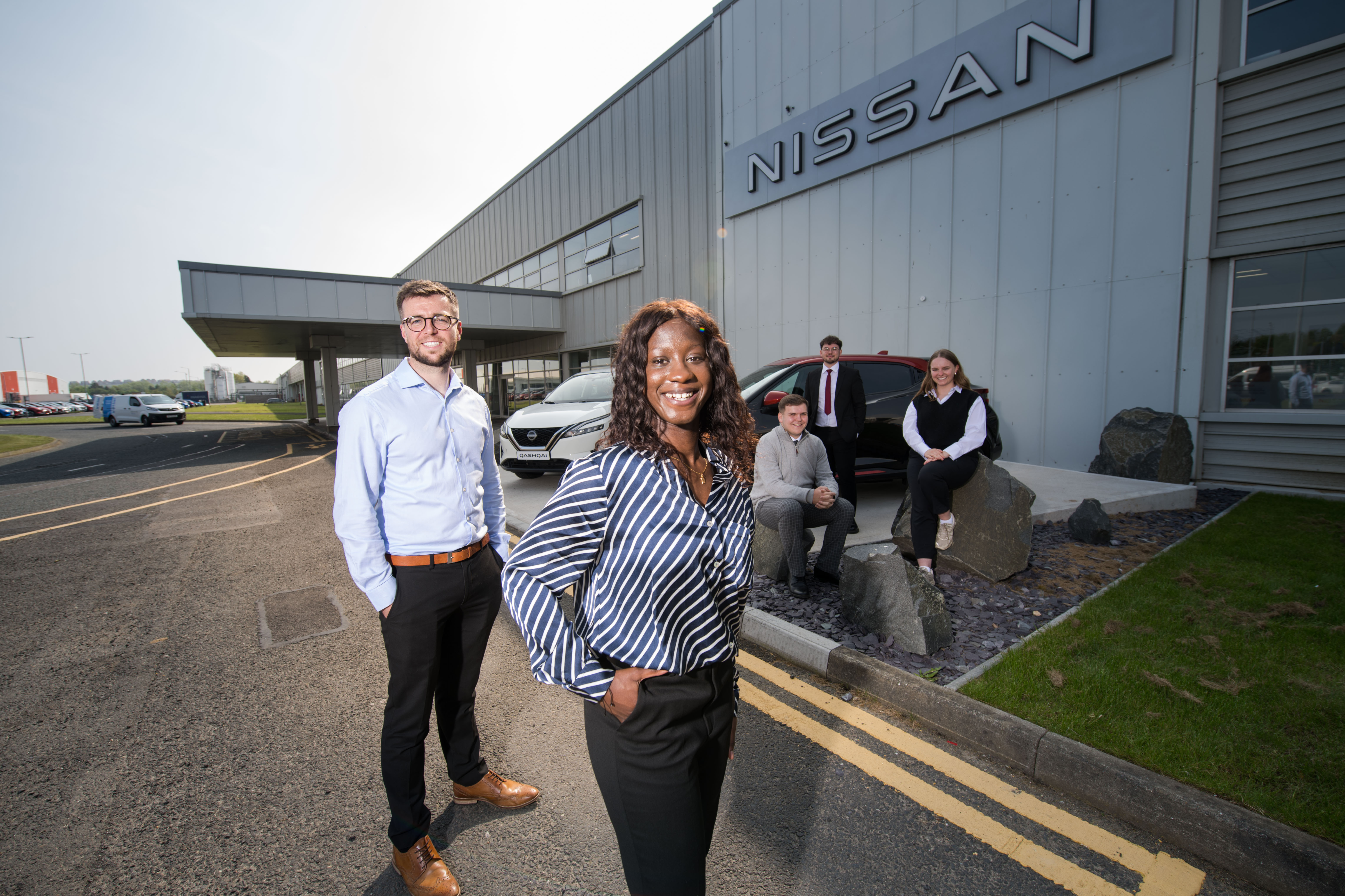 Image of 5 people dressed smart smiling at the camera outside a Nissan dealership