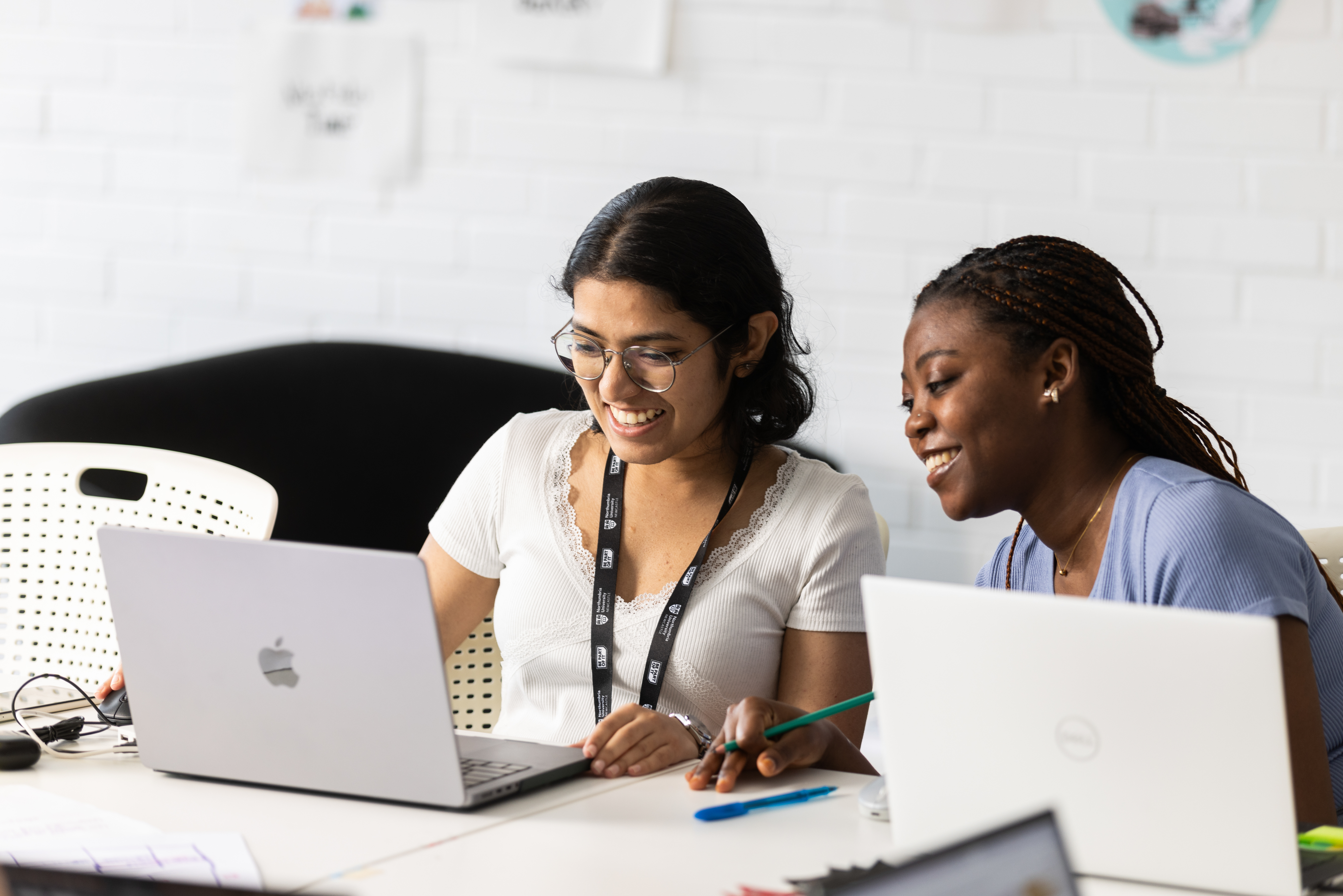 2 female students working together and smiling at their laptop