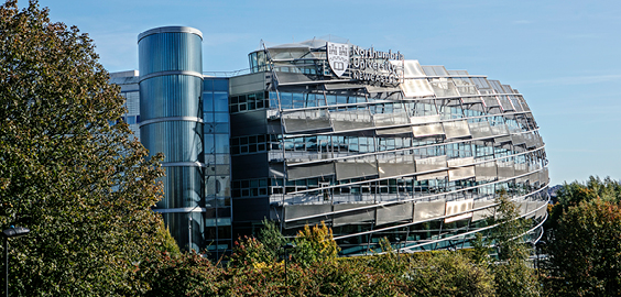 an image of the universitys city campus east building with trees in the foreground and blue sky in the background
