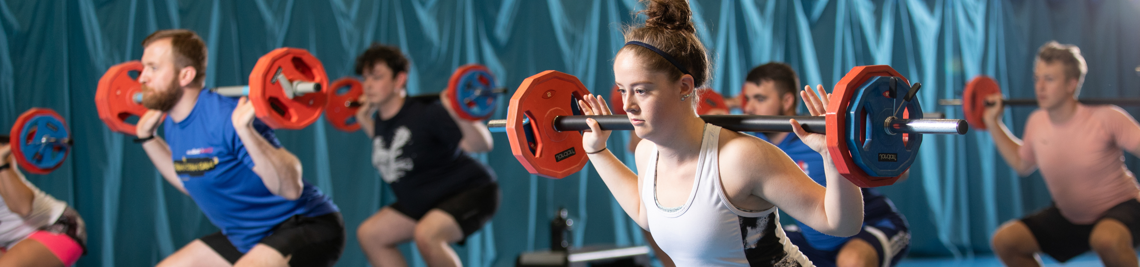 a young woman in a fitness class lifts a barbell and weights on her shoulders