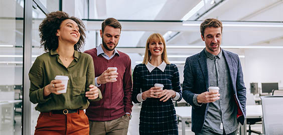 Four people walking in the same direction talking to each other and holding coffee cups in an office setting