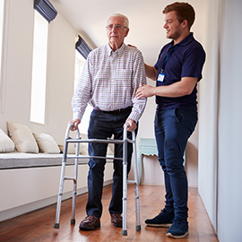 Senior man using a walking frame with male nurse at home