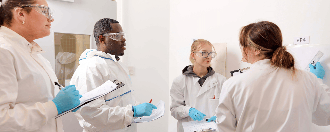 students working together dressed in white coats with safety glasses and blue gloves on