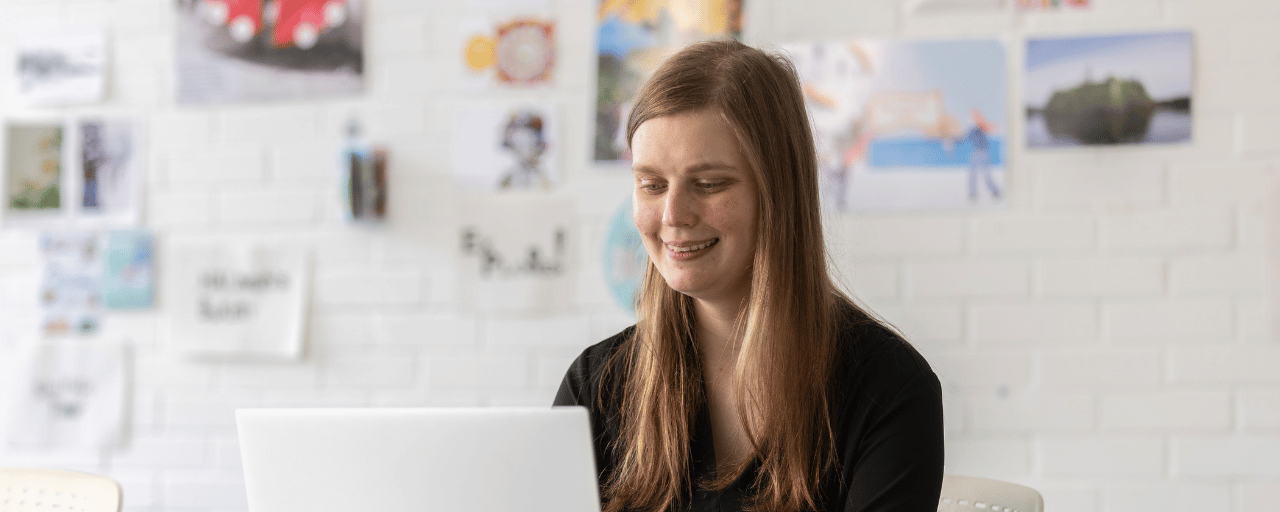 student smiling whilst working on laptop