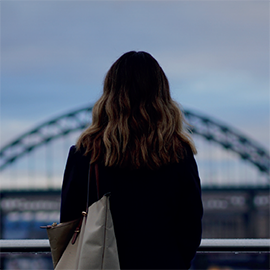 Close-up of an individual with a handbag, looking out onto the Gateshead Millenium Bridge.