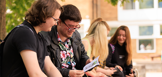 2 people sitting and reading a booklet with 3 girls in the background, all smiling