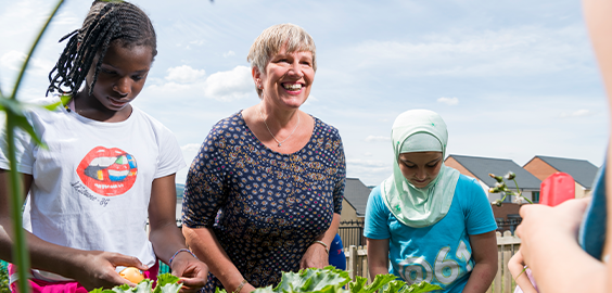 A group of people, including children and an older woman, gardening together on a sunny day.