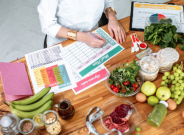 person writing in a meal planner surrounded by vegetables