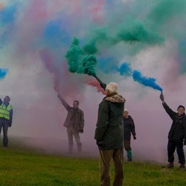 people holding colourful smoke in field