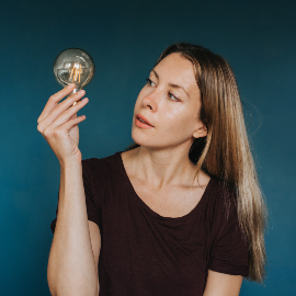 A woman holding a gold light bulb and looking at it curiously