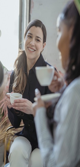 Two women looking at each other both holding coffee mugs and smiling