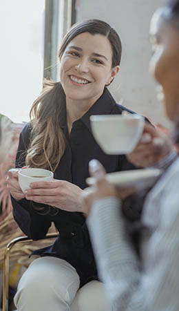 Two women looking at each other both holding coffee mugs and smiling