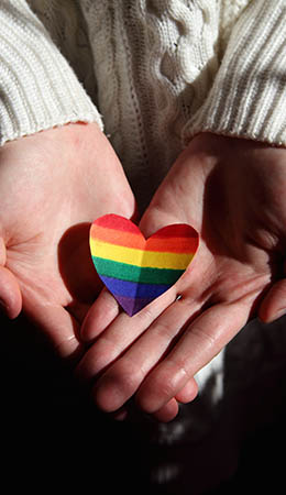 A LGBTQ+ heart flag on two open female hands