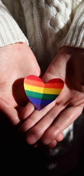 A LGBTQ+ heart flag on two open hands