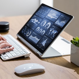 A person typing on a keyboard attached to a portable screen displaying different graphs and charts 