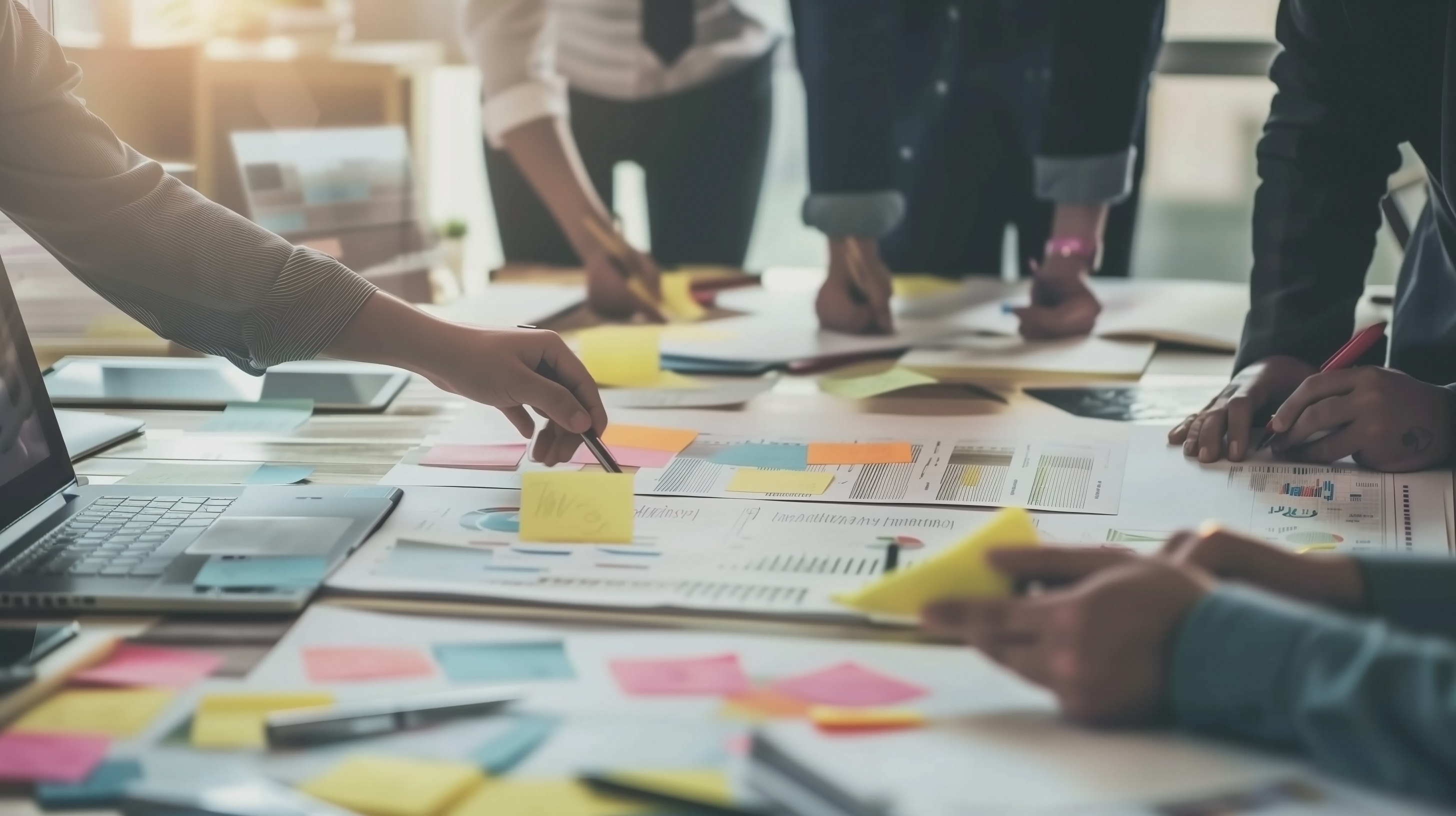 Colleagues leaning across a table pointing at documents and placing multiple coloured post it notes on areas