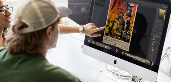 Two students looking at a computer screen with one pointing at it.