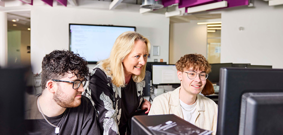 Two students working on computers with support from lecturer in a seminar setting