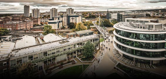 Picture of Northumbria University City Campus. You can see multiple buildings across the skyline as the picture is taken from the roof of a building. The main focus is the courtyard which has people walking through it.