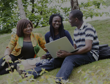 Nigerian students studying and talking together. The students are sitting on the grass with their laptops.