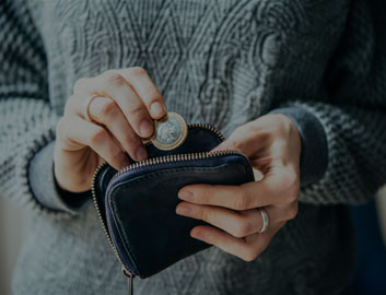 Person putting coins into a purse, wearing a grey jumper