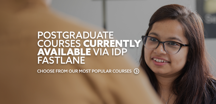 Female student sat, looking at another student and smiling. There is text embedded on the image that reads: "Postgraduate courses currently available via IDP FastLane"