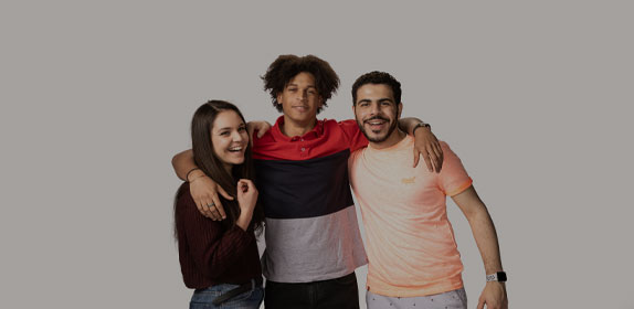 Three students smiling with their arms round each others shoulders 