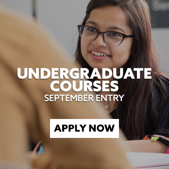 Close-up of an India stduent sat a desk and smiling at someone off-camera. There is text embedded on the image that reads: "Undergraduate courses for September entry. Apply now."