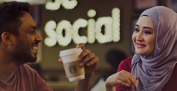 Close-up of two international students sat inside the Students' Union, laughing and holding cups of coffee.