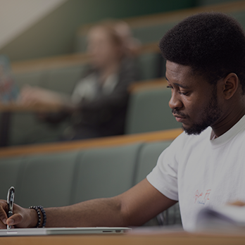 Close-up of a student taking notes in a lecture theatre.