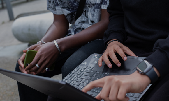 Close-up of students using a laptop - one of the students is also holding a phone.