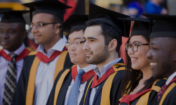 Close-up of six students of varying nationalities that are posing for a group photo at Congregation. They are stood outside in the sun, smiling and wearing their graduation cap and gowns.