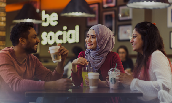 Three international students sat in the Student's Union, talking and laughing. They are gatghered round a table and all have Starbucks drinks.