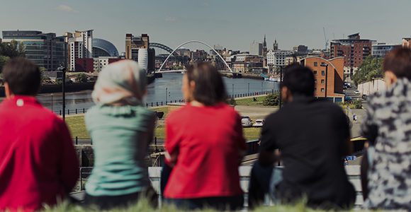 Close-up of five students sat with their backs to the camera, looking over Newcastle Quayside on a sunny day.