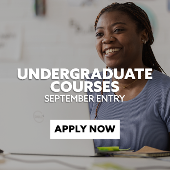 Female student sat at her laptop in a workshop, laughing. There is text embedded on the image that reads: "Undergraduate Courses for September Entry - Apply now"