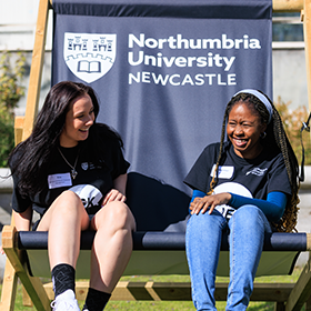 Two students sat in a giant Northumbria-branded deck chair on an Open Day.