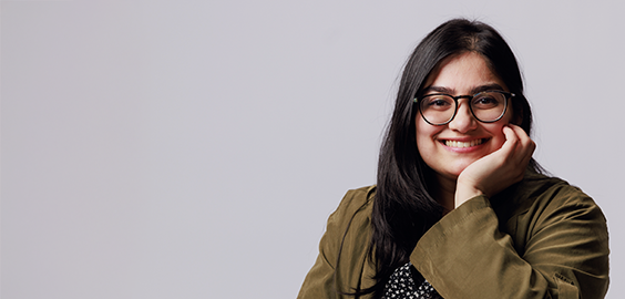 Student of South Asian decent sat smiling, looking directly at the camera as part of the 'I Am Northumbria' photoshoot campaign.