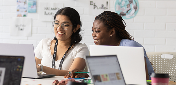 Two students sat in a classroom, working collaboratively over a laptop.