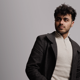 Image of a male student wearing a long coat, against a white background as part of the 'I Am Northumbria' campaign.