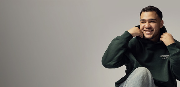 Image of a male student sat on the floor and smiling, against a white background as part of the 'I Am Northumbria' campaign.