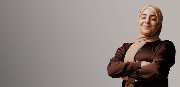 Image of a female student with her arms crossed, smilling and with a head covering on, against a white background as part of the 'I Am Northumbria' campaign.