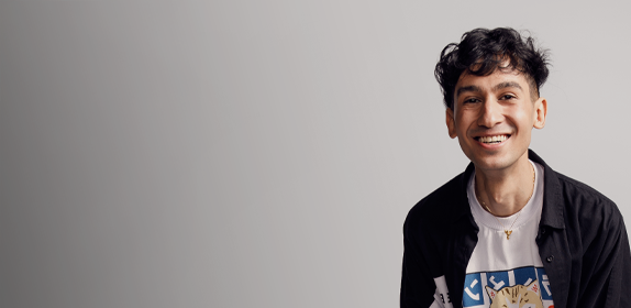 Image of a student with dark hair and graphic t-shirt, smiling against a white background as part of the 'I Am Northumbria' campaign.
