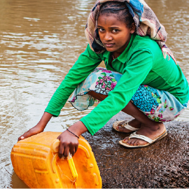 Young girl collecting water from a river