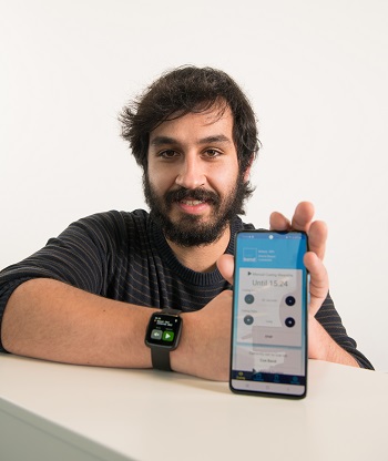 Caption:Senior research assistant Luís Carvalho pictured wearing the Cue Band device on his wrist and holding a mobile phone with the Cue Band app open on the screen